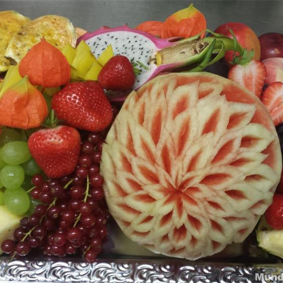 Geschnitzte Wassermelone mit Blütenmuster, umgeben von Obst